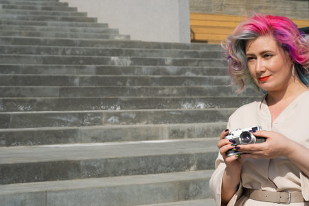 Caucasian woman with curly colored hair takes pictures on an old retro camera outdoors.