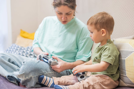 Caucasian woman teaches her little son to play console. Joystick in hands
