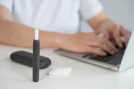 A woman smokes an electronic cigarette while working on a laptop. Tobacco heating systemの写真素材