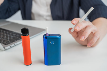 A woman demonstrates different types of cigarettes. An e-cigarette, a disposable vape, and a regular cigaretteの写真素材