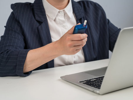 Business woman smoking an electronic cigarette while working on a laptop. Tobacco heating system