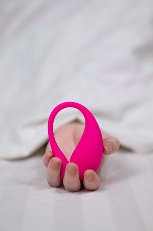 Woman holding curved pink vibrator while lying in bedの写真素材
