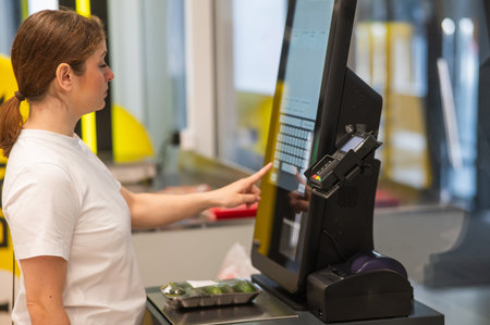 A woman weighs cucumbers at a self-service checkoutの写真素材