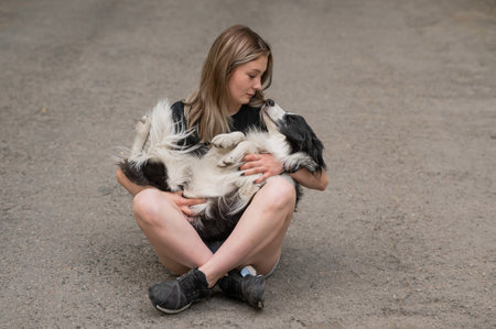 Young caucasian woman sitting on asphalt and hugging border collie dog