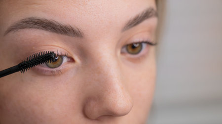 Close-up of a young woman intently applying mascara to her eyelashes