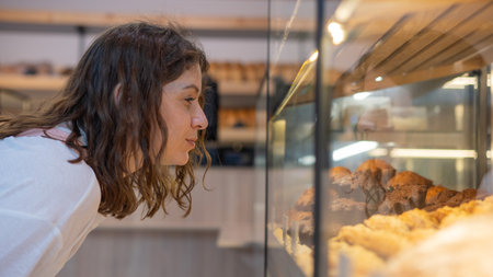 Caucasian woman looks greedily at baked goods in a bakeryの写真素材