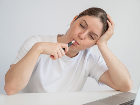 Tired woman smoking an electronic cigarette while working on a laptop.の写真素材