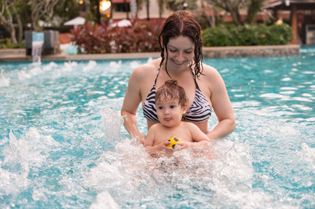 Caucasian woman holds her son while swimming in a pool on vacation. Mom teaches little boy to swimの写真素材
