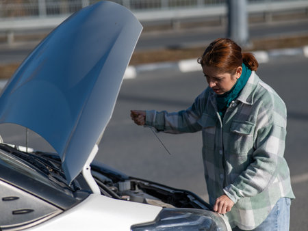 Caucasian female driver checking oil level in car engineの写真素材