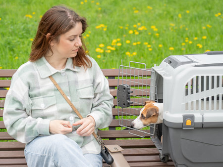 Owner sits on bench with Jack Russell Terrier in cage for safe travelの写真素材