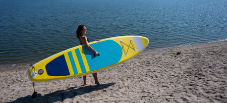 Caucasian woman walks along the beach and carries a sup board on the river in the city. Summer sportの写真素材