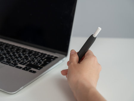A woman smokes an electronic cigarette while working on a laptop. Tobacco heating systemの写真素材