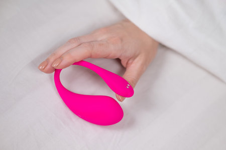 Woman holding curved pink vibrator while lying in bedの写真素材