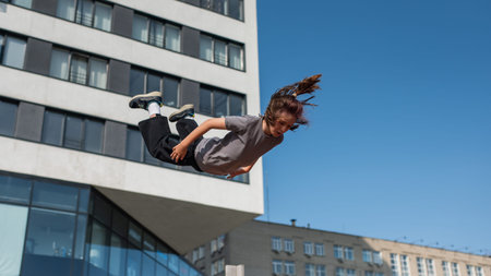 A girl jumps in the air with her legs spread and arms outstretched, showcasing her joy and...