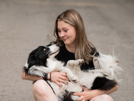 Young caucasian woman sitting on asphalt and hugging border collie dogの写真素材