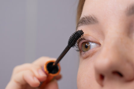 Close-up of a young woman intently applying mascara to her eyelashesの写真素材