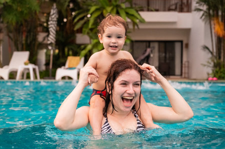 Caucasian woman holds her son while swimming in a pool on vacation. Mom teaches little boy to swimの写真素材