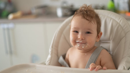 Cute baby boy smeared in sour cream sits in a high chair