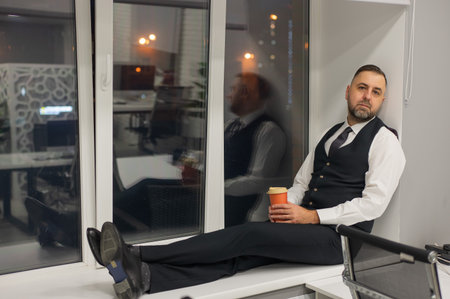 Thoughtful Caucasian man sitting on windowsill in officeの写真素材