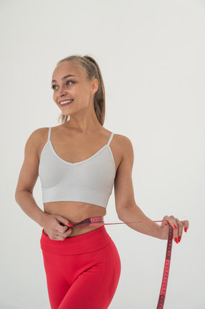 Young woman measuring her waist on white backgroundの写真素材