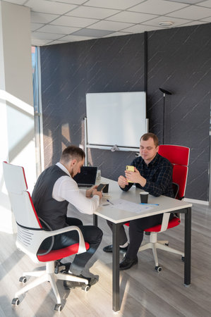 Two Caucasian men using smartphones while sitting at a deskの写真素材