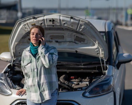Caucasian woman calls on the phone and asks for help while standing near a car with an open hood