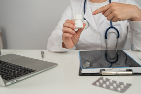 Doctor with bracelet holding pills and typing on laptop. Concept of hormone therapy for gender reassignmentの写真素材