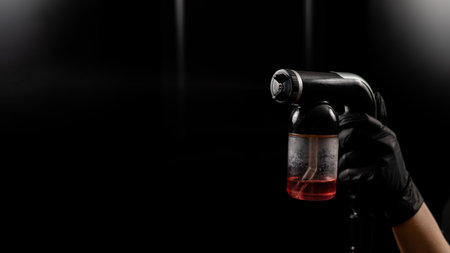 Close-up of instant tanning equipment in the hands of a master. Gun spraying paint for leather against black background.の写真素材