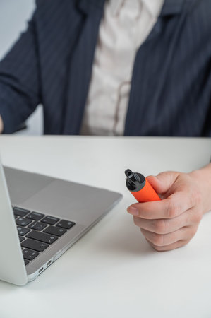 Faceless businesswoman smokes disposable vape and works on laptop