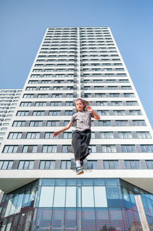 A girl jumps on a trampoline in front of a tall building