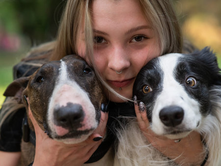 This heartwarming image captures a person joyfully holding two affectionate dogs close to their...