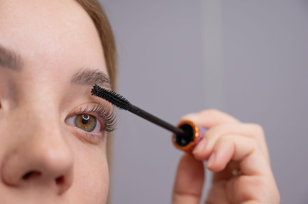 Close-up of a young woman intently applying mascara to her eyelashesの写真素材