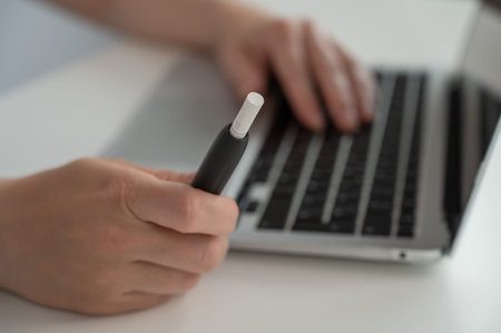 A woman works on a laptop while holding an electronic cigarette.の写真素材