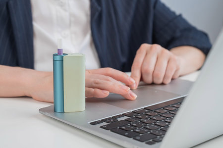 Business woman smoking an electronic cigarette while working on a laptop. Tobacco heating system