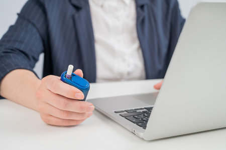 Business woman smoking an electronic cigarette while working on a laptop. Tobacco heating systemの写真素材