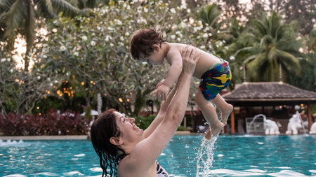 Caucasian woman holds son while swimming in pool on vacation