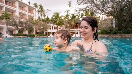 Caucasian woman holds her son while swimming in a pool on vacation. Mom teaches little boy to swim