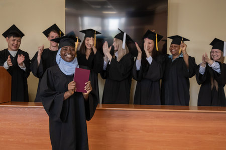 Happy African woman in hijab receiving diploma and classmates applauding her