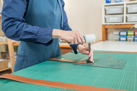 Woman tanner processes the edges of a leather belt in a workshop