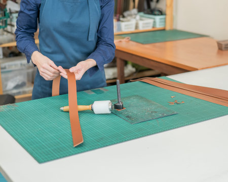Woman tanner processes the edges of a leather belt in a workshop