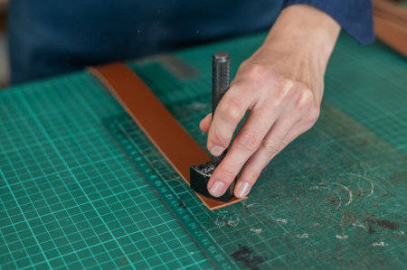 Woman tanner processes the edges of a leather belt in a workshop