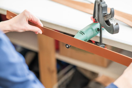 Leatherworker grinding the edge of a strip of leather for a belt in the workshop