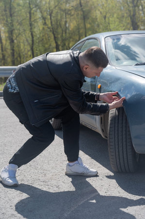 Caucasian man examines and tries to fix a deformation on the body of his car