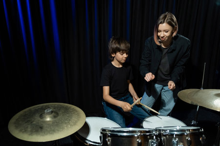 Young woman teaches a boy to play the drums in the studio on a black background. Music school...