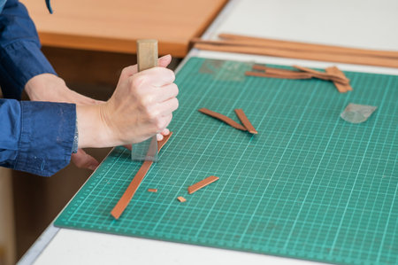 Woman tanner processes the edges of a leather belt in a workshopの写真素材