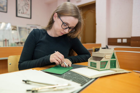 Caucasian young woman making a model of a building. Student of the construction university