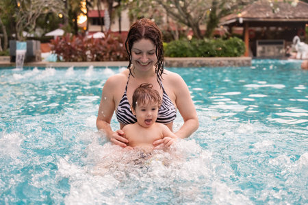 Caucasian woman holds her son while swimming in a pool on vacation. Mom teaches little boy to swimの写真素材