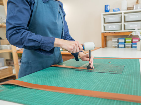 Woman tanner processes the edges of a leather belt in a workshop
