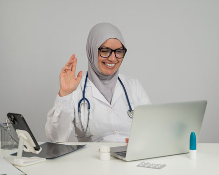 Female doctor in hijab talking to patient via video link on laptopの写真素材