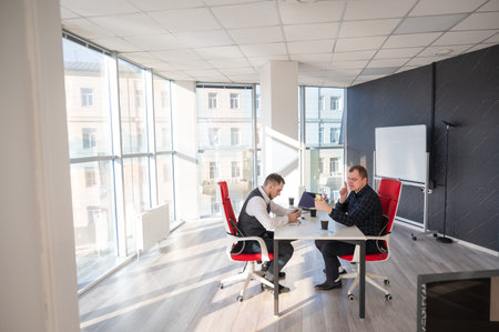 Two Caucasian men using smartphones while sitting at a deskの写真素材